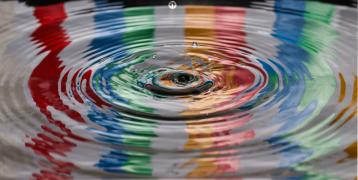 Drop of water falling into water reflecting colours